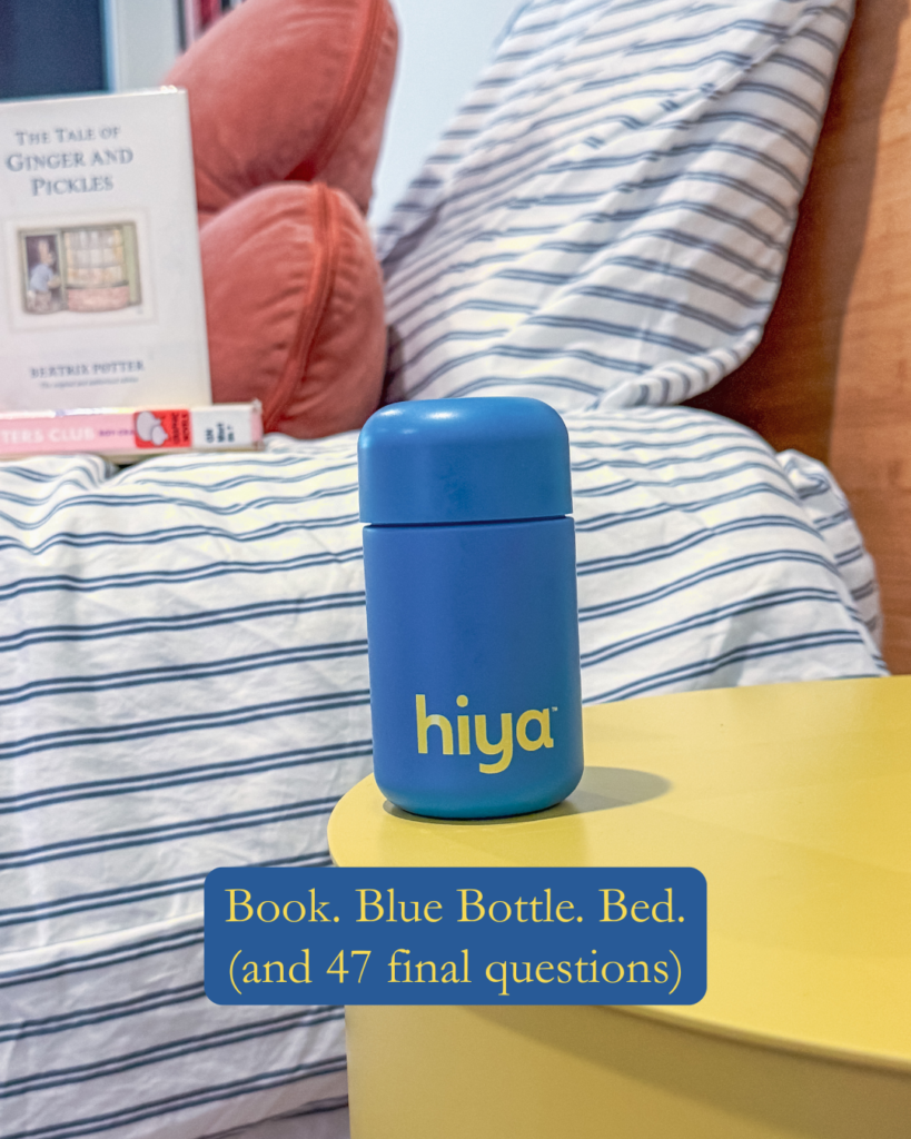 A blue hiya bottle sits on a yellow table near a bed with striped bedding. A book titled The Tale of Ginger and Pickles and red pillow are visible in the background.